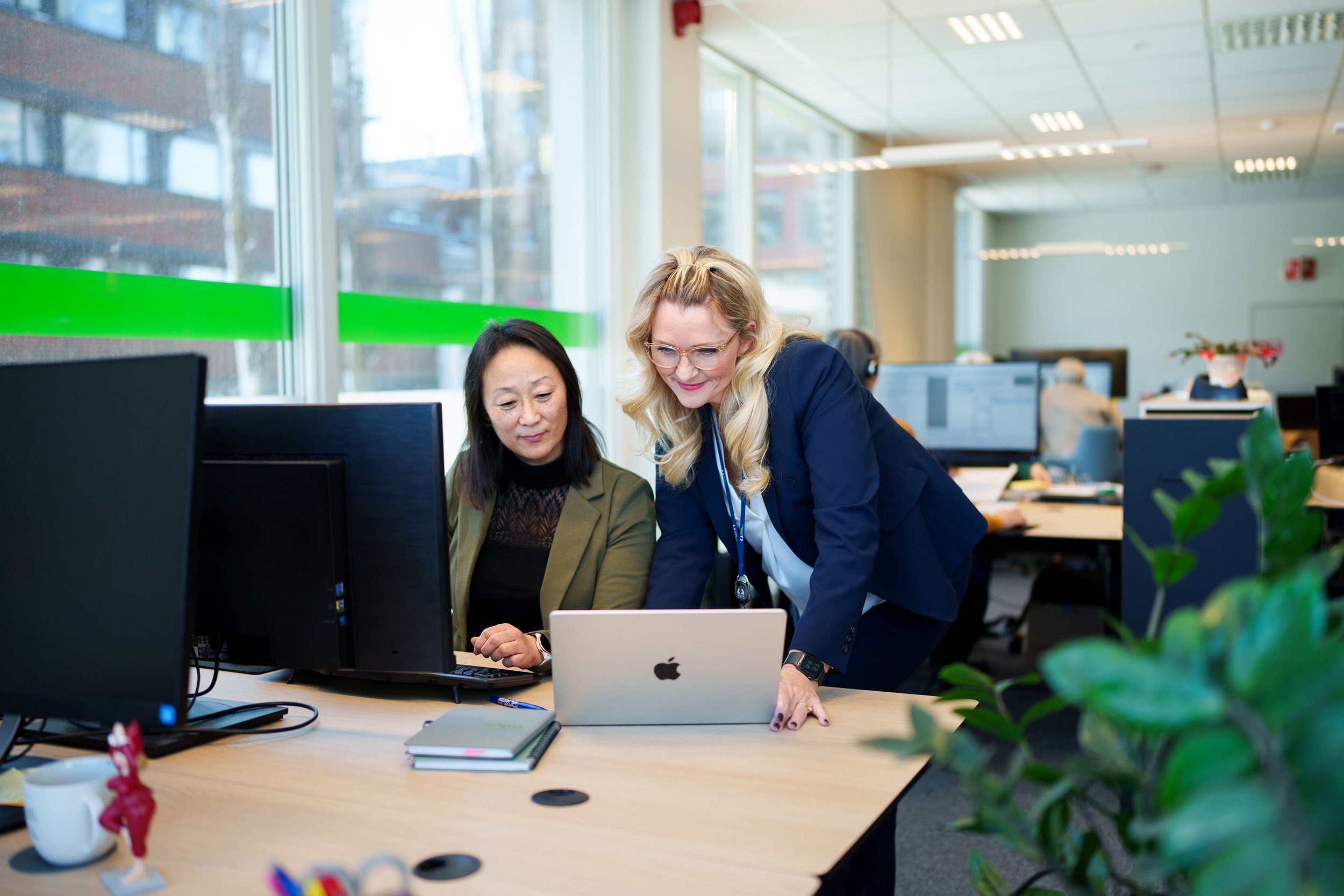 To ansatte som sitter i kontorlandskap og prater over en PC